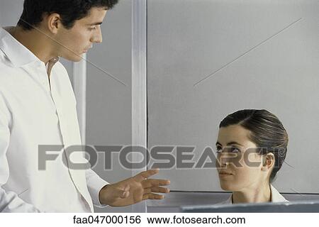Stock Photograph - Man standing, talking to female colleague. Fotosearch