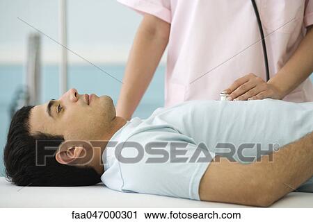 Stock Image - Nurse listening to man's chest with stethoscope, cropped. Fotosearch