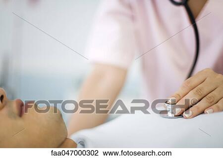 Stock Image - Nurse listening to patient's heart using stethoscope, cropped. Fotosearch