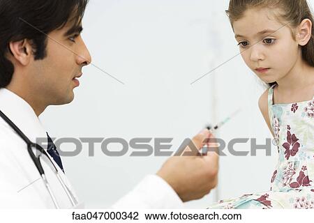 Stock Image - Pediatrician showing little girl syringe. Fotosearch