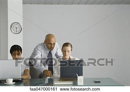 Professional man standing behind young female colleague, pointing at her computer screen View Large Photo Image Stock Image - Professional man standing behind young female colleague, pointing at her computer screen. Fotosearch