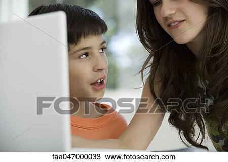 Stock Image - Sister and younger brother using laptop computer together. Fotosearch