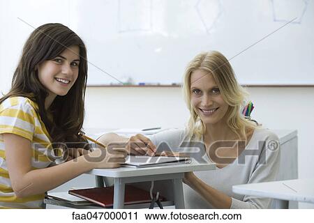 Stock Image - Teacher assisting student, both smiling at camera. Fotosearch