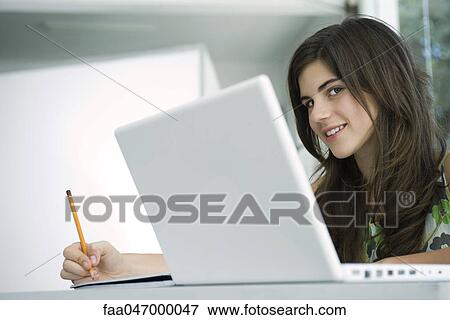 Stock Photo - Teenage girl at desk writing, laptop computer in foreground. Fotosearch