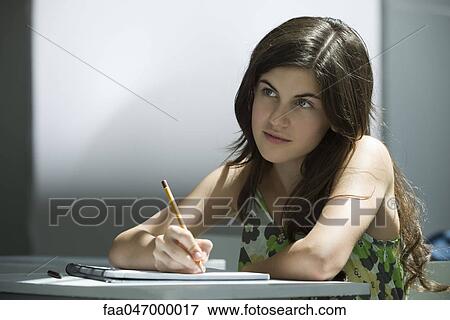 Stock Photo - Teenage girl writing in notebook, contemplatively looking away. Fotosearch