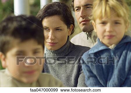 Stock Photo - Woman sitting outdoors with husband and children, looking away in thought. Fotosearch