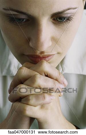 Stock Image - Woman with hands clasped in front of chin, close-up. Fotosearch
