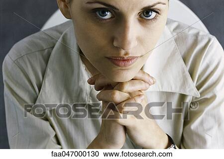 Stock Image - Woman with hands clasped under chin, looking at camera, high angle view. Fotosearch