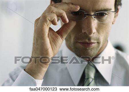 Stock Image - Young businessman adjusting glasses, portrait. Fotosearch