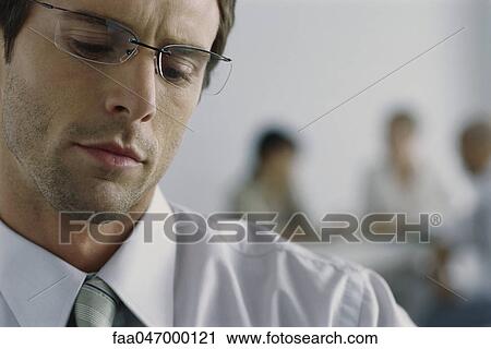 Stock Image - Young businessman wearing glasses, looking down with furrowed brow. Fotosearch