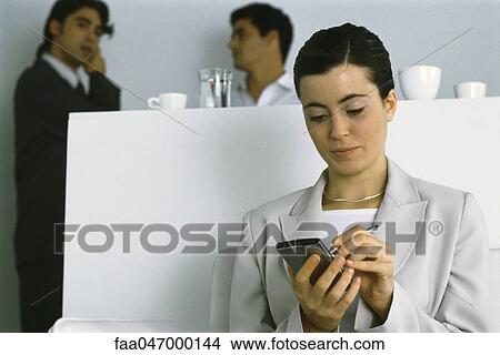 Young businesswoman using PDA while colleagues chat in background View Large Photo Image Picture - Young businesswoman using PDA while colleagues chat in background. Fotosearch
