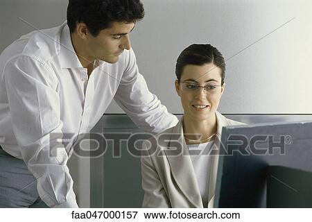 Stock Photo - Young professional woman smiling, looking at computer screen while male colleague leans over her shoulder. Fotosearch