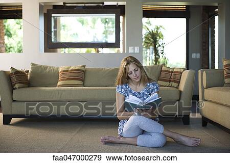 Stock Photo - Young woman sitting on living room floor reading book. Fotosearch