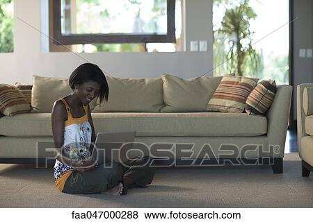 Stock Photo - Young woman sitting on living room floor using laptop computer. Fotosearch