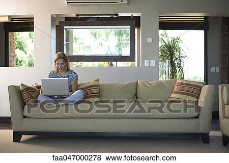 Young woman sitting on sofa using laptop computer View Large Photo Image Stock Photo - Young woman sitting on sofa using laptop computer. Fotosearch