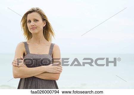 Blonde woman standing with arms folded, sea in background, looking at camera, waist up View Large Photo Image Picture - Blonde woman standing with arms folded, sea in background, looking at camera, waist up. Fotosearch