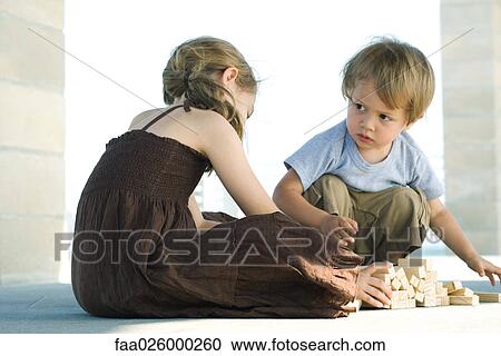 Stock Image - Boy and girl sitting on floor, playing with building blocks. Fotosearch