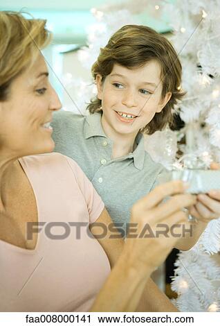 Boy handing mature woman present next to Christmas tree View Large Photo Image Stock Image - Boy handing mature woman present next to Christmas tree. Fotosearch