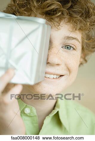 Boy holding up present in front of face View Large Photo Image Stock Photo - Boy holding up present in front of face. Fotosearch