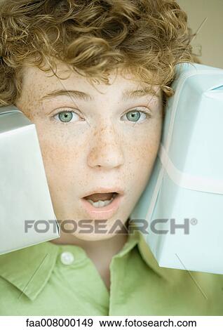 Stock Photo - Boy holding up presents on either side of face. Fotosearch