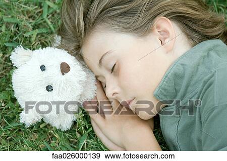 Boy lying in grass with eyes closed, head resting on teddy bear View Large Photo Image Stock Photo - Boy lying in grass with eyes closed, head resting on teddy bear. Fotosearch