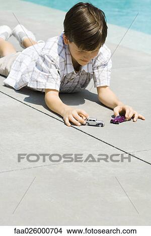 Boy lying on ground, playing with toy cars, next to pool View Large Photo Image Picture - Boy lying on ground, playing with toy cars, next to pool. Fotosearch