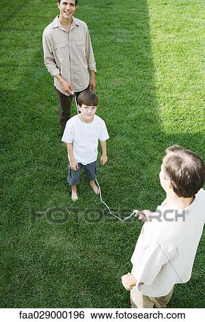 Stock Photograph - Boy playing jump rope with two men, smiling at camera. Fotosearch