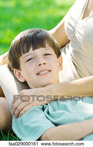 Stock Image - Boy resting head on mother's lap, smiling at camera, close-up. Fotosearch
