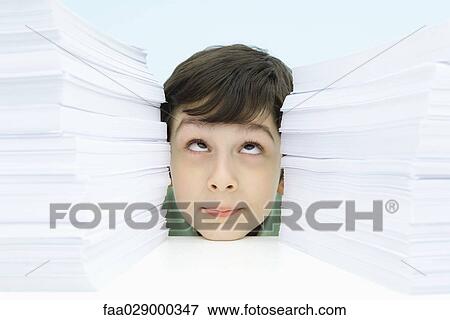 Stock Photo - Boy resting head on table between two stacks of paper, rolling eyes. Fotosearch