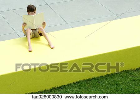 Boy sitting on low wall outdoors, reading book, high angle view View Large Photo Image Stock Image - Boy sitting on low wall outdoors, reading book, high angle view. Fotosearch