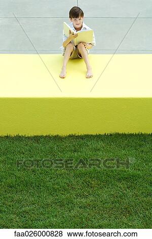 Boy sitting on low wall outdoors, holding book, looking away, high angle view View Large Photo Image Stock Photo - Boy sitting on low wall outdoors, holding book, looking away, high angle view. Fotosearch