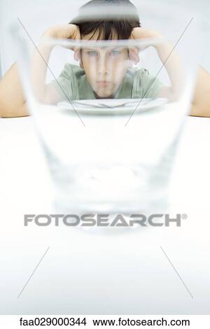 Boy sulking at table, looking at camera through water glass View Large Photo Image Picture - Boy sulking at table, looking at camera through water glass. Fotosearch