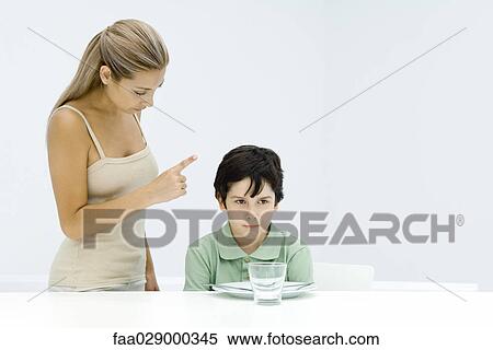 Boy sulking at table, mother standing beside him, shaking her finger View Large Photo Image Stock Photography - Boy sulking at table, mother standing beside him, shaking her finger. Fotosearch