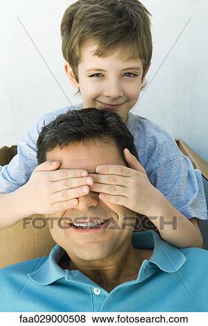 Boy with hands over his father's eyes, looking at camera, both smiling View Large Photo Image Stock Photo - Boy with hands over his father's eyes, looking at camera, both smiling. Fotosearch