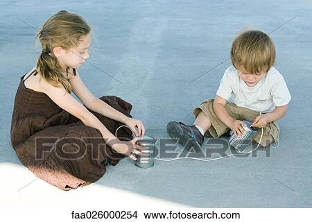 Brother and sister sitting on the ground, playing with tin can phone View Large Photo Image Picture - Brother and sister sitting on the ground, playing with tin can phone. Fotosearch