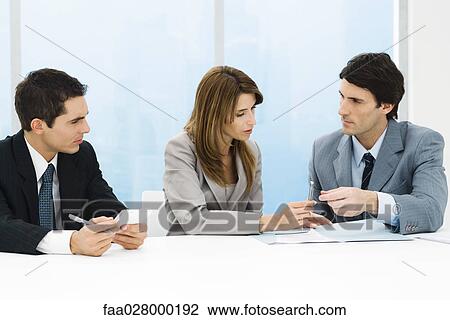 Stock Image - Business associates seated together at table, discussing document, woman handing man pen. Fotosearch