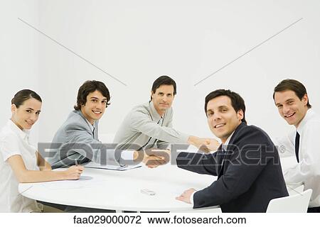 Stock Image - Business associates shaking hands across table, smiling at camera. Fotosearch