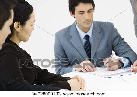 Business associates sitting at table, one man signing document View Large Photo Image Stock Image - Business associates sitting at table, one man signing document. Fotosearch