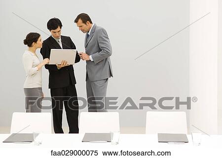 Business associates standing in conference room, looking at laptop computer together View Large Photo Image Stock Photography - Business associates standing in conference room, looking at laptop computer together. Fotosearch