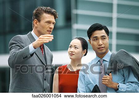 Picture - Business associates standing outdoors, talking, man gesturing with hand. Fotosearch