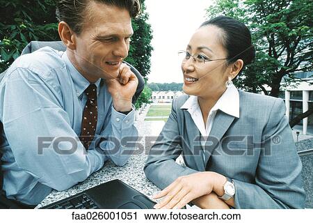 Business partners sitting outdoors, smiling, woman using laptop computer View Large Photo Image Stock Image - Business partners sitting outdoors, smiling, woman using laptop computer. Fotosearch