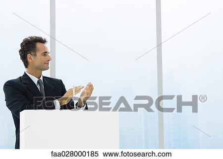 Businessman at lectern clapping hands, looking away, smiling View Large Photo Image Stock Photography - Businessman at lectern clapping hands, looking away, smiling. Fotosearch