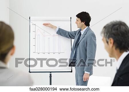 Picture - Businessman giving presentation to colleagues, pointing at graph, side view. Fotosearch