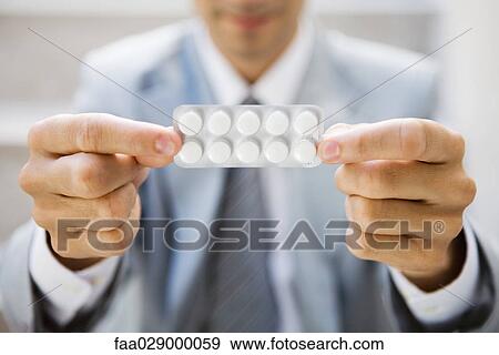 Stock Photo - Businessman holding out medicine in blister pack, focus on foreground, cropped view. Fotosearch
