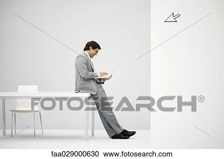 Stock Image - Businessman leaning against desk, using laptop computer, cursor graphic in foreground. Fotosearch
