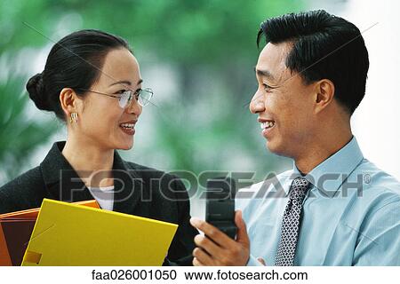 Stock Image - Businessman showing cell phone to female colleague, both smiling at each other. Fotosearch