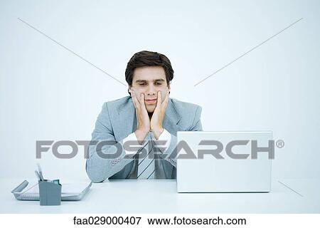 Businessman sitting at desk, holding head in hands, frowning View Large Photo Image Stock Photo - Businessman sitting at desk, holding head in hands, frowning. Fotosearch