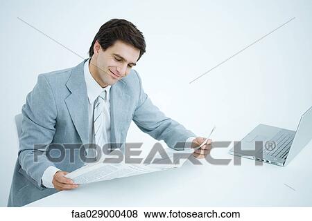 Stock Photo - Businessman sitting at desk, reading newspaper. Fotosearch