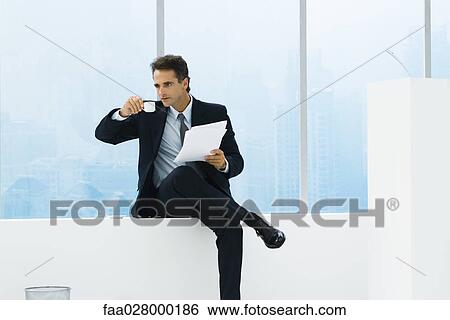 Businessman sitting in windowsill next to lectern, holding papers, drinking coffee View Large Photo Image Stock Photograph - Businessman sitting in windowsill next to lectern, holding papers, drinking coffee. Fotosearch