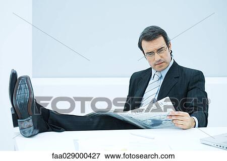 Stock Photo - Businessman sitting with feet up, reading newspaper. Fotosearch